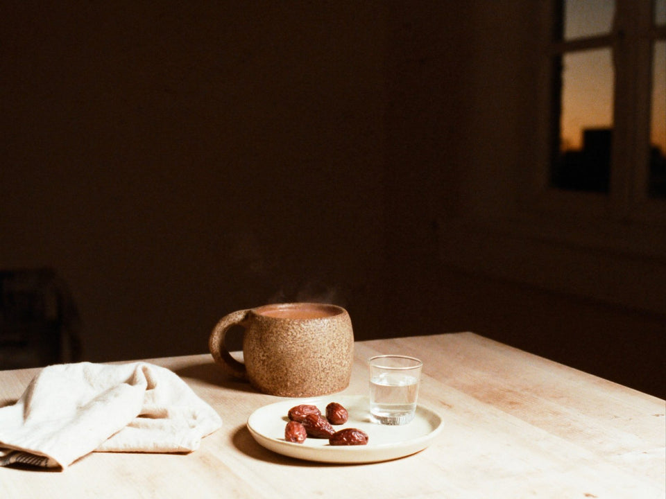 A mug of bone broth beside a small plate of dates on a wooden table