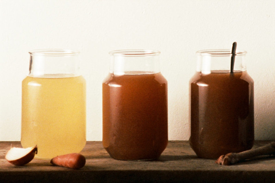 Three glass jars in a row holding broth, stock and bone broth, lightest to darkest