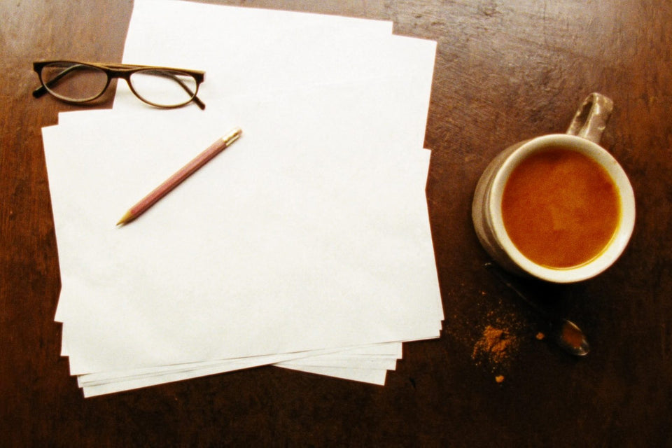 A mug of bone broth on a wooden desk beside a stack of papers, a pencil and reading glasses