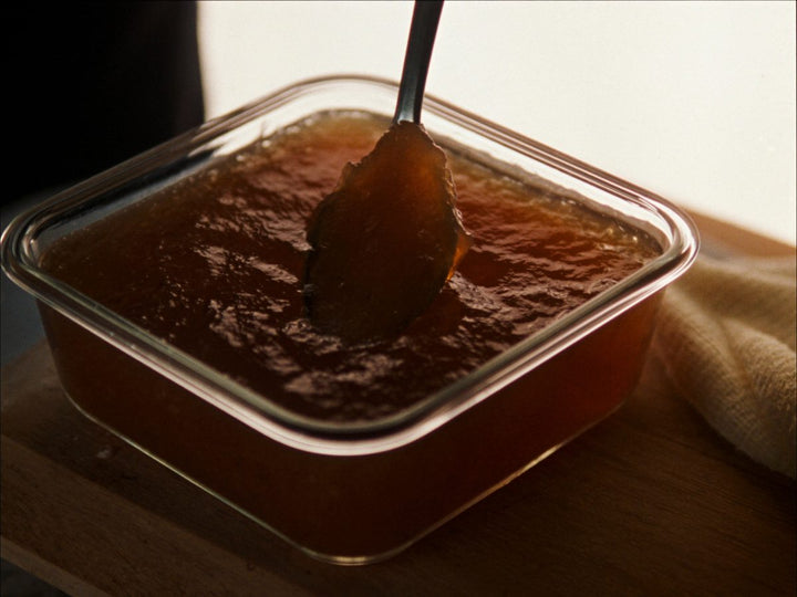 A spoon pressed into chilled bone broth that has set to a firm jelly in a glass dish