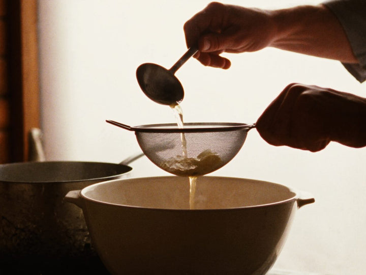 Bone broth being poured through a fine sieve into a bowl